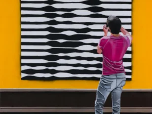Painting with a rear-facing figure viewing black and white striped art in yellow and blue surroundings.
